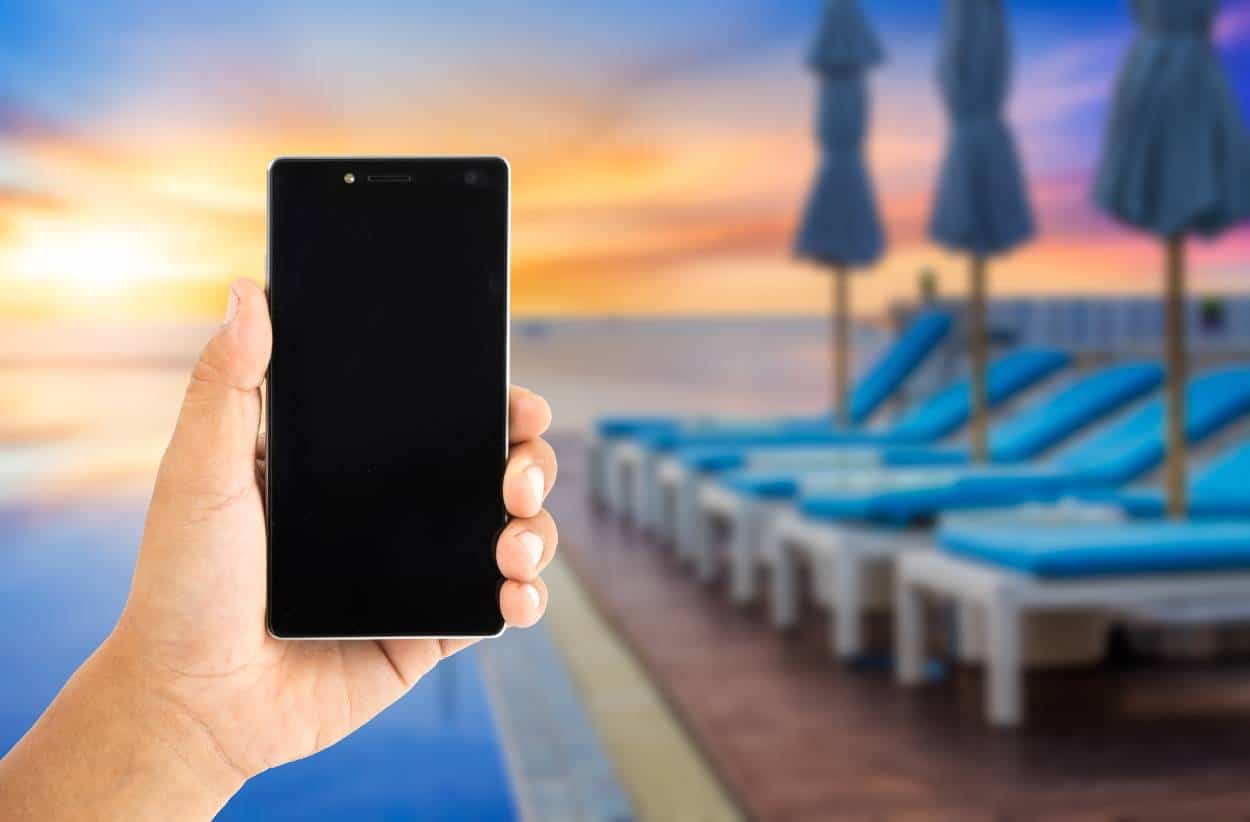 Image of person holding a smart phone with pool and loungers in background
